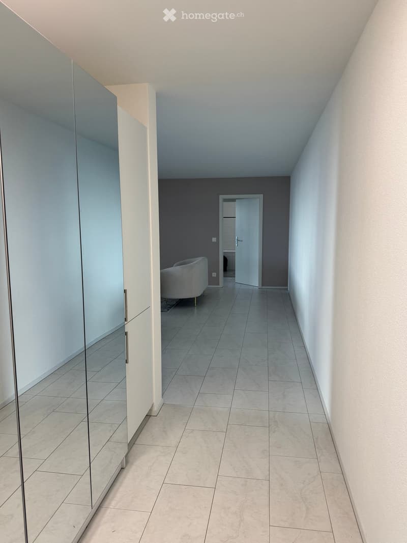 Empty hallway with white tiles, large mirror, and a door at the end.