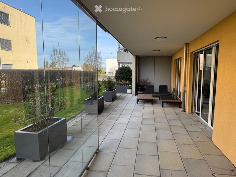 covered terrace with seating area and potted plants, tiled flooring, glass walls, view of green lawn