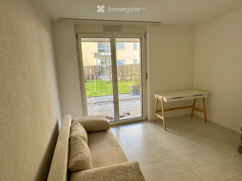 Empty living room with sliding doors, couch, desk, tile flooring.