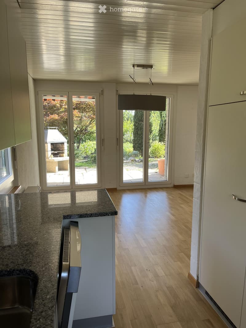 Modern kitchen with light wooden flooring, granite countertop, and large sliding glass doors leading to a garden area.