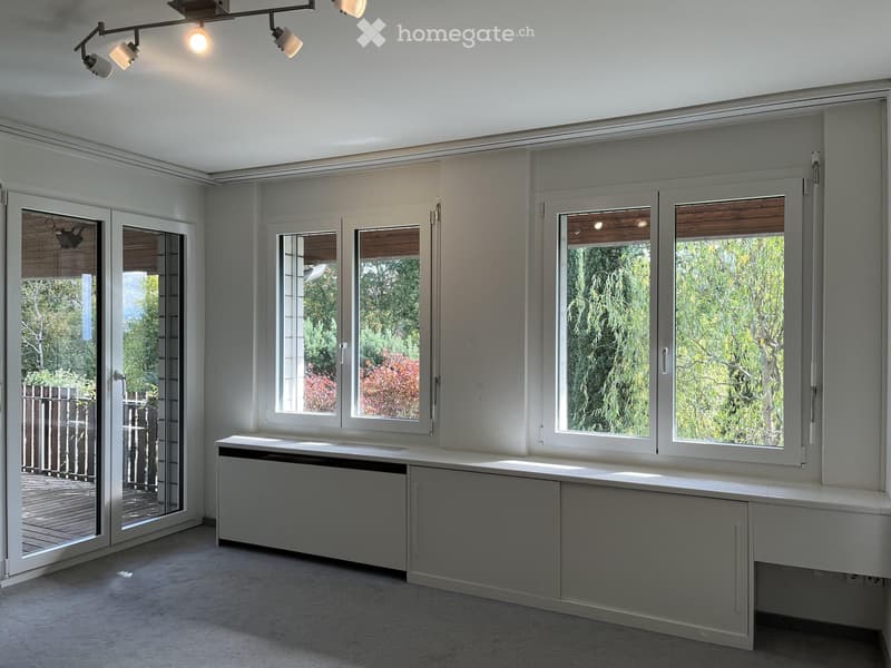 Empty room with large windows, built-in bench seating, and modern lighting fixtures.