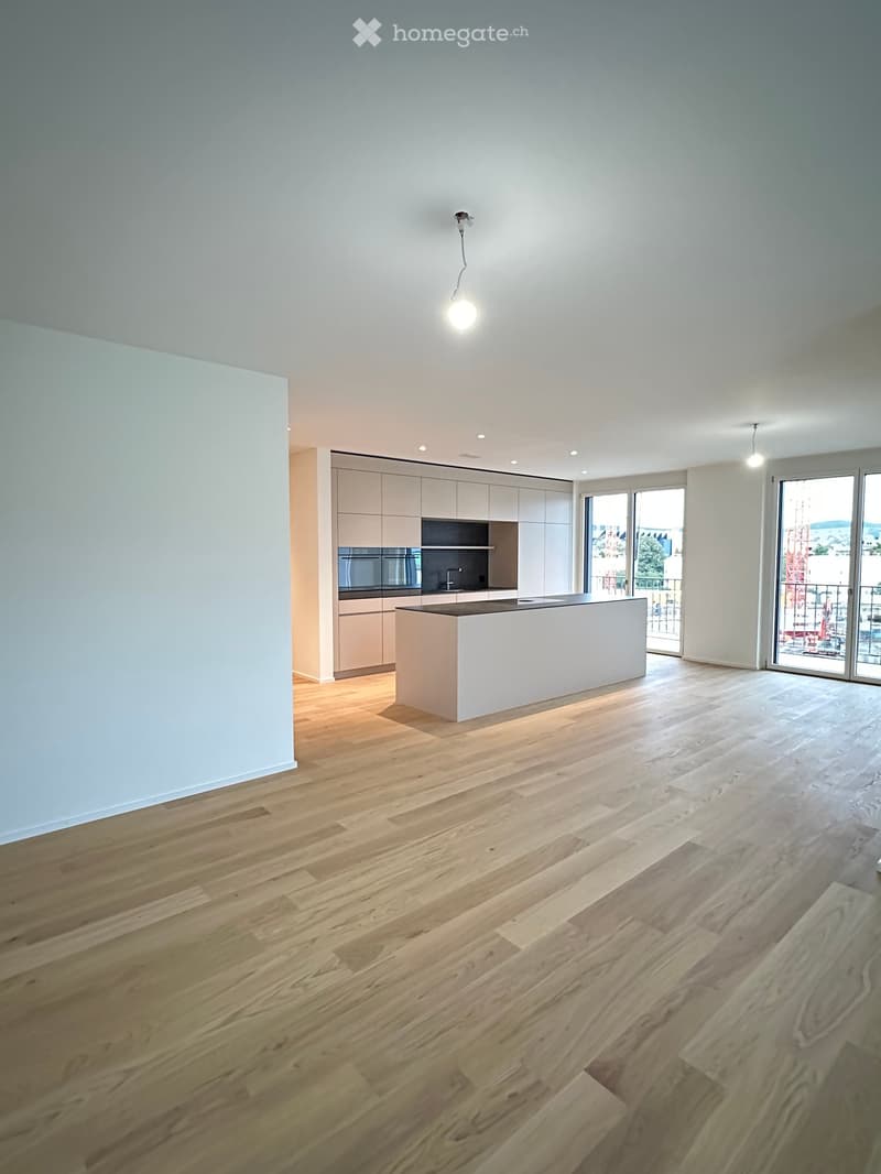 Modern kitchen with light wood flooring, white cabinetry, and a central island. Large windows provide natural light and a view of the city.