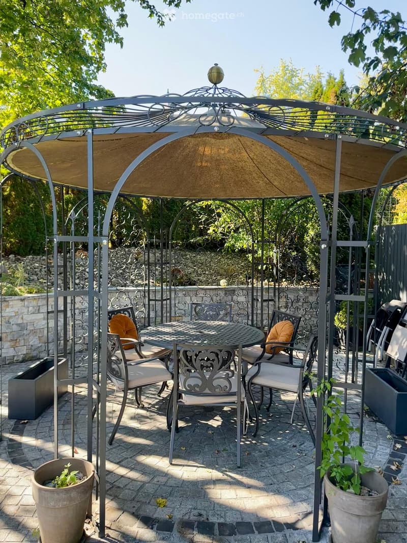Outdoor patio with a metal gazebo, round table, four chairs, and potted plants.