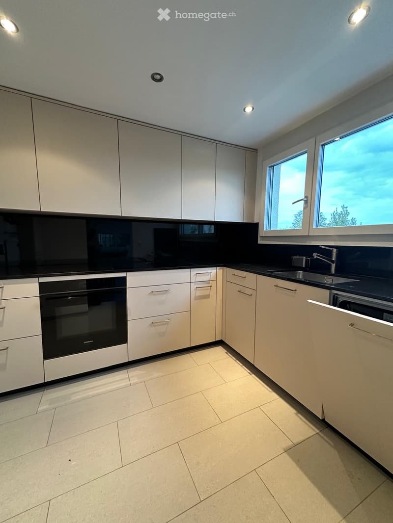 Modern kitchen with white cabinets, black countertops, and built-in appliances including an oven and sink.