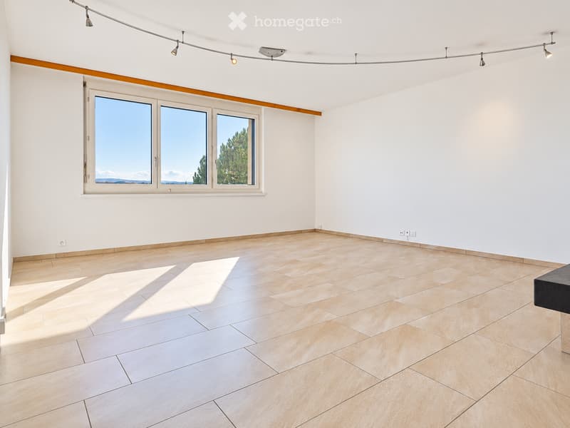 Empty room with light-colored tiled flooring, white walls, large windows with a scenic view, and recessed lighting fixtures.