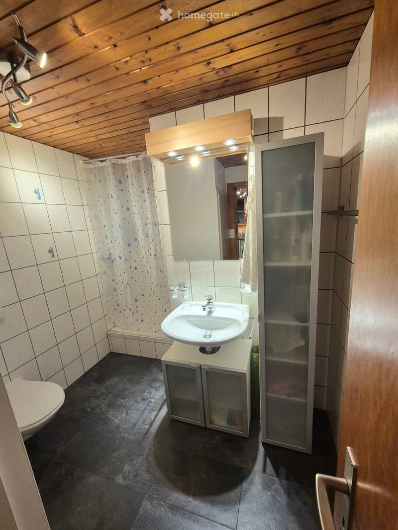 Bathroom with a wooden ceiling, tiled walls, a sink with a mirror, a shower with a curtain, and a toilet.