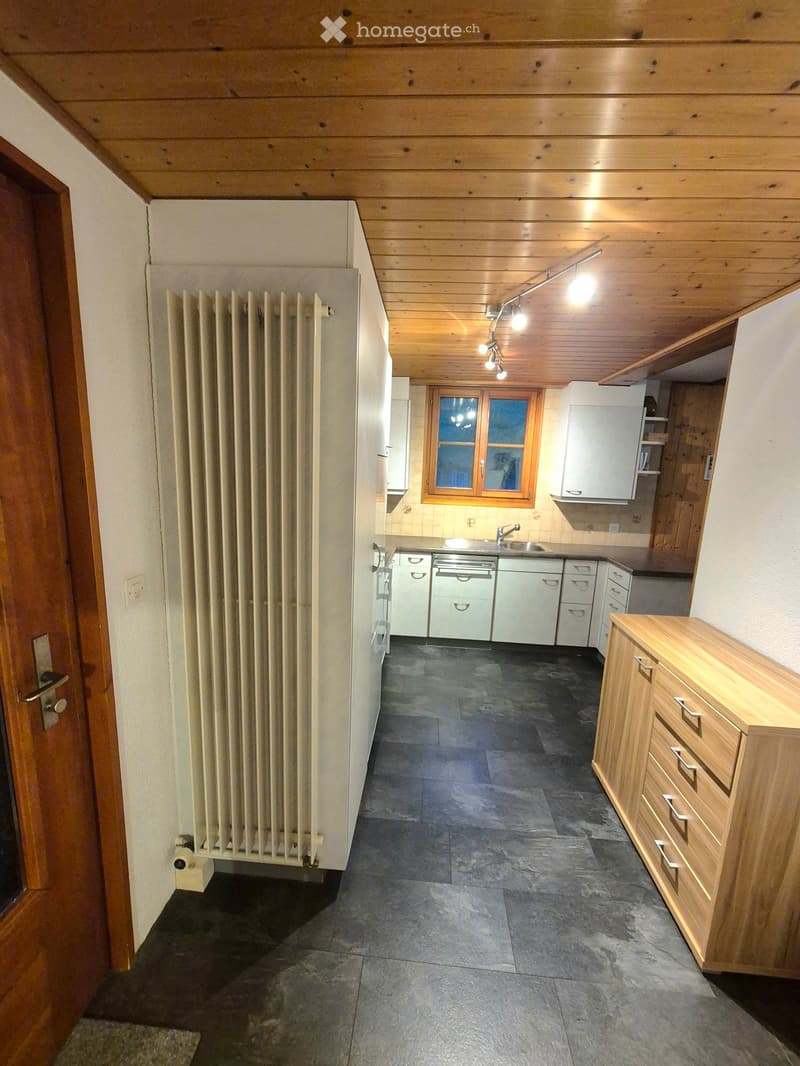 Kitchen with wooden ceiling, dark tiled floor, white cabinets, sink, and radiator.