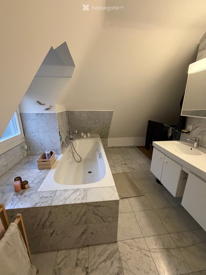 Modern bathroom with a freestanding bathtub, marble tiles, a sink with a mirror, and a small wooden crate holding toiletries.