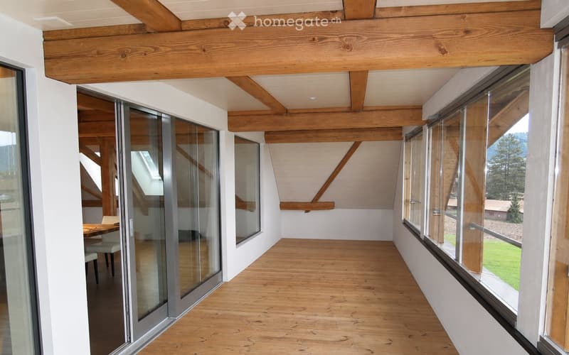 Bright hallway with wooden beams and large windows, leading to a dining area with a table and chairs.