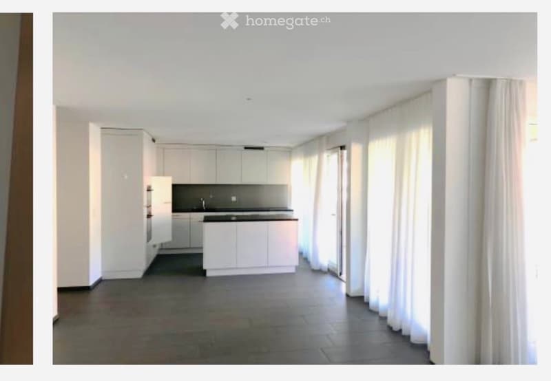 Modern, minimalist kitchen with white cabinets, a central island, and a dark countertop. The space is bright with large windows and sheer curtains.