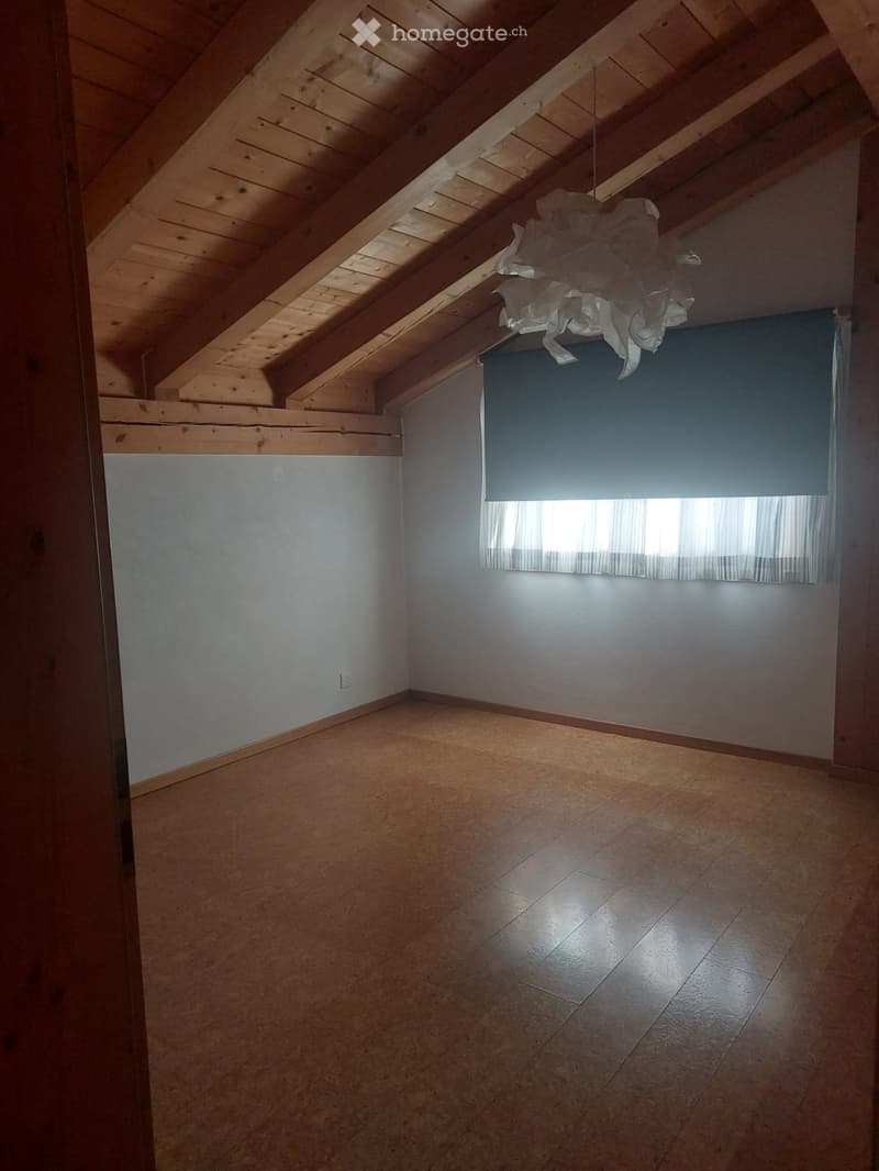 Empty attic space with wooden beams, tiled floor, and a window with curtains.