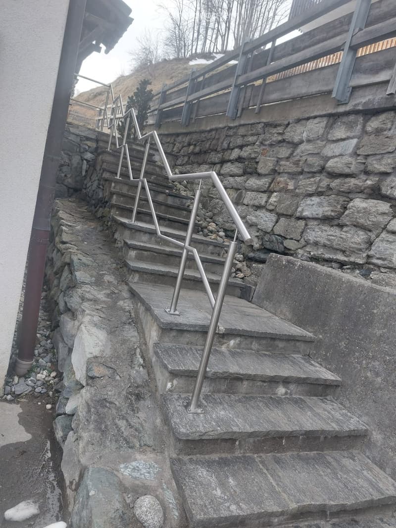 Stone staircase with metal railings leading up a steep incline, flanked by a stone wall and wooden deck above.