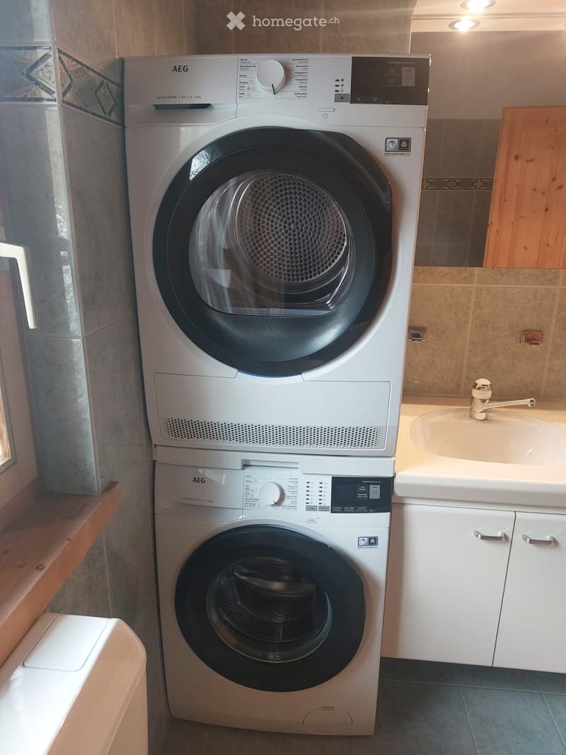 Bathroom with a stacked washing machine and dryer unit, a sink with a faucet, and white cabinetry.