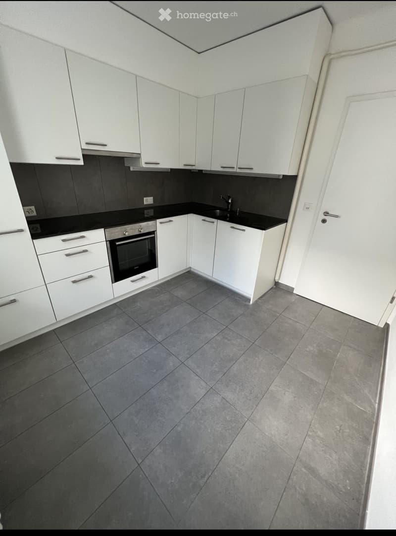 Modern kitchen with white cabinets, black countertops, grey tiled floor, and stainless steel oven and sink.