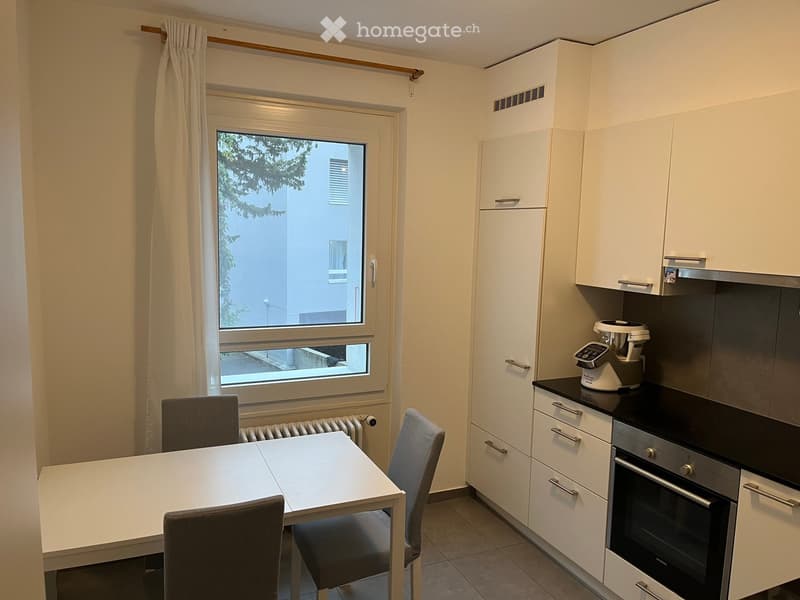 Modern kitchen with white cabinets, a dining table with chairs, and a window overlooking a building.