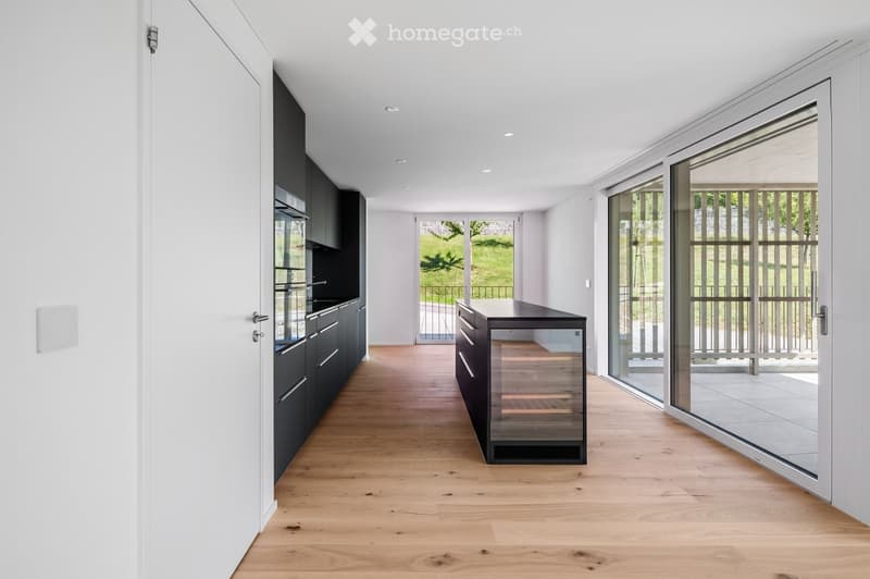 Modern kitchen with dark cabinets, light wooden flooring, and a wine rack in the center. Large glass doors lead to an outdoor area.
