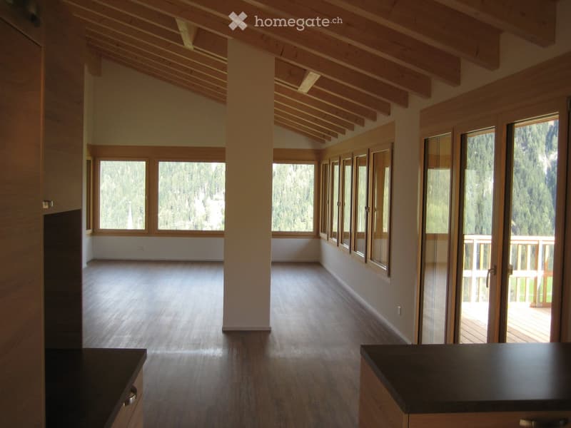 Open, unfurnished room with wooden floors, exposed wooden beams, large windows, and a balcony area with a wooden deck.