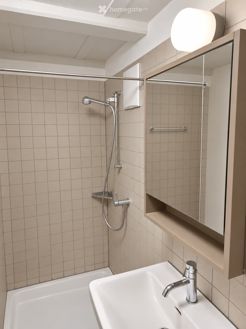 Modern bathroom with a bathtub, sink, and shower area. Features a large mirror with built-in storage, sleek chrome fixtures, and beige tiled walls.
