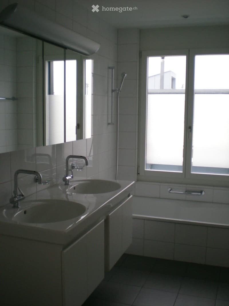 Modern bathroom with two sinks, a bathtub, and a showerhead, featuring large windows and tiled walls.