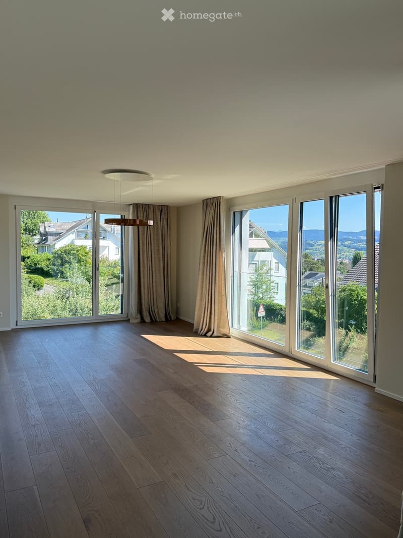 Empty room with wooden flooring, large windows, and modern lighting fixtures. The space is well-lit with natural light streaming in from the windows.