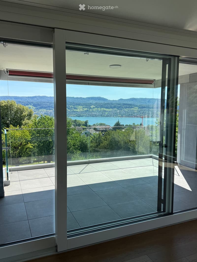 Modern balcony with large glass doors, tiled floor, and scenic view of a lake and mountains.