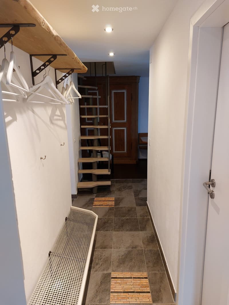 narrow hallway with coat rack, spiral staircase, tiled floor, wooden wardrobe, small desk, light fixtures