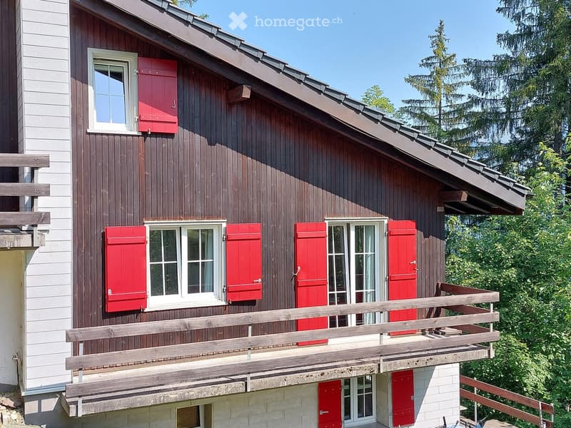 Red wooden shutters, sloped roof, raised wooden balcony, brown wooden exterior
