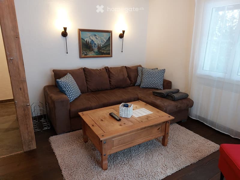 white walls, beige carpet, white couch, wooden coffee table, white remote control, light fixtures, picture frame on the wall, white curtains