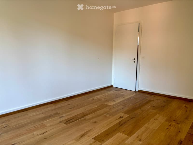 Empty room with light wooden flooring and white walls, featuring a single white door.