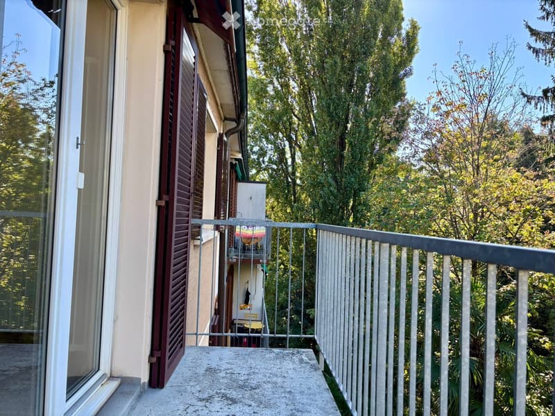 Balcony with metal railing, overlooking a lush green garden area with trees and plants.