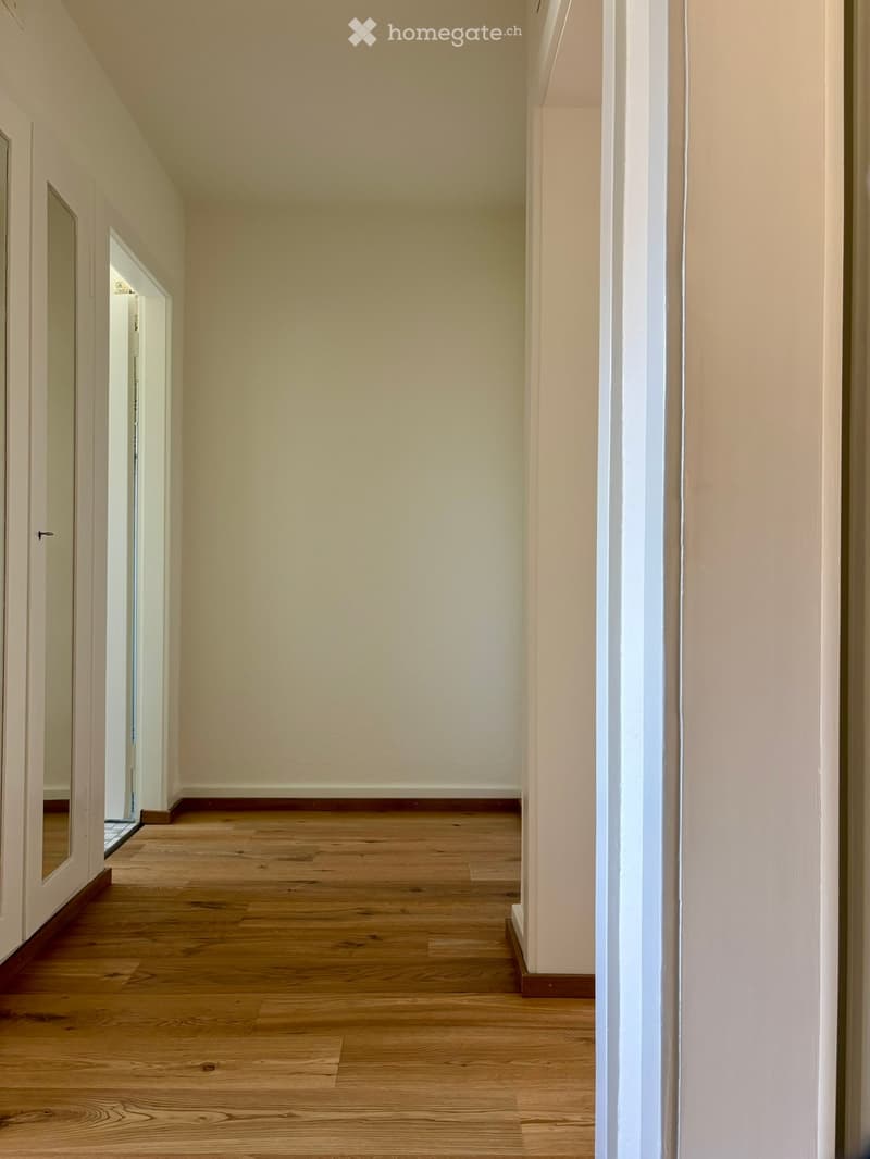 Empty hallway with wooden flooring, white walls, and open doors leading to other rooms.