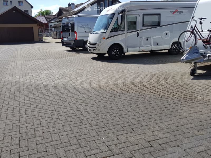 Brick-paved parking area with a large motorhome, a smaller van, and a bicycle on a trailer.