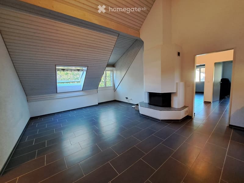 Empty room with dark tiled floor, white walls, and a built-in fireplace. The room features a slanted wooden ceiling and a skylight window.