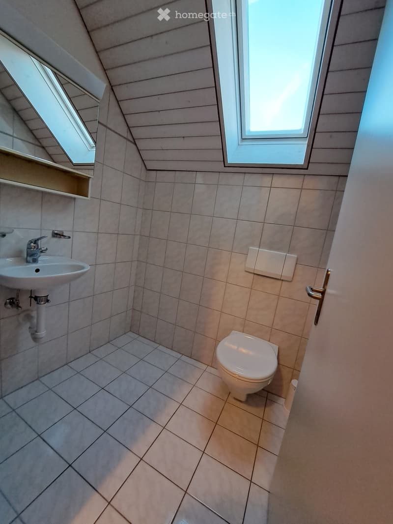 Small bathroom with tiled walls and floor, featuring a toilet, sink, and window with blinds.
