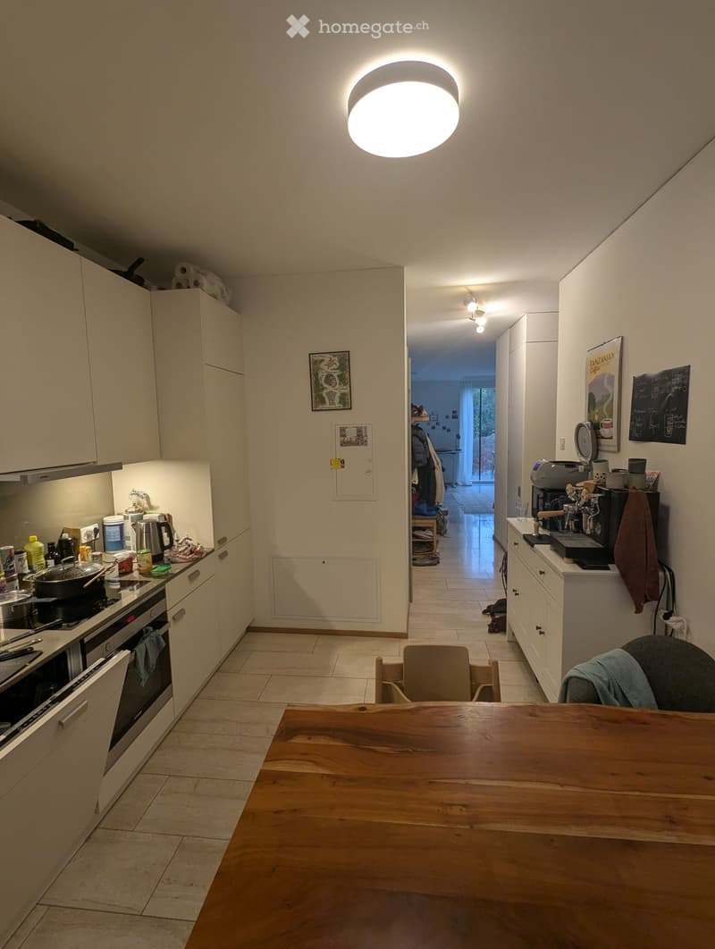 Modern kitchen with white cabinets, a wooden dining table, and various appliances including an oven, coffee maker, and a kitchen island.