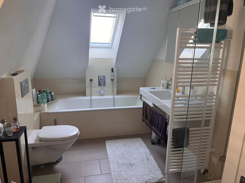 Modern bathroom with a bathtub, toilet, sink, mirror, towel rack, and decorative items on a small table.