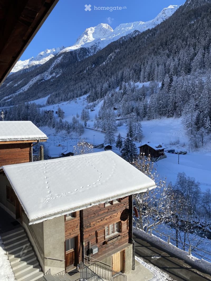 Snow-covered mountain view from a balcony, with wooden chalets and a clear blue sky.