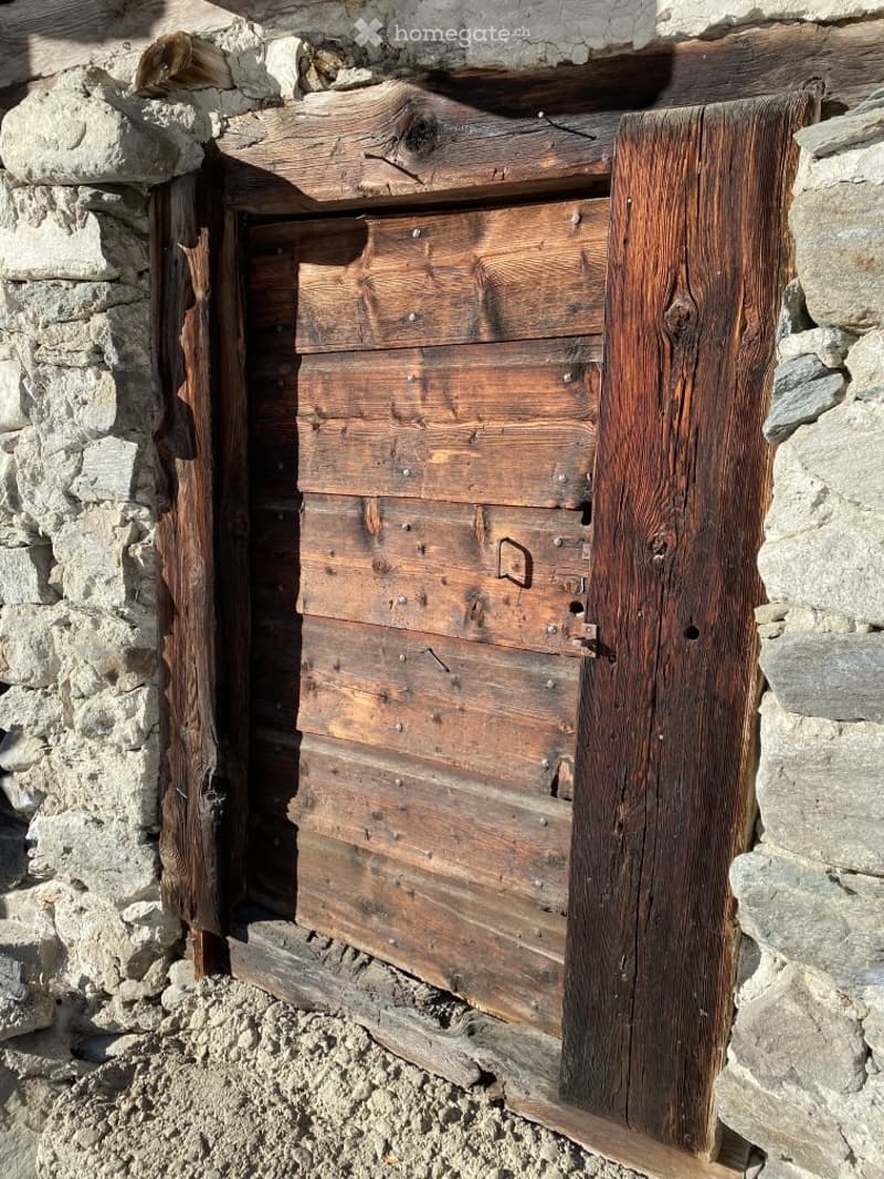 A rustic wooden door set into a stone wall, featuring weathered planks and metal hinges.