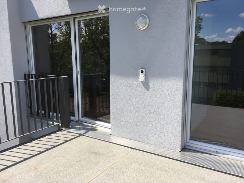 Balcony with modern sliding glass doors, metal railing, and a light fixture on the wall.
