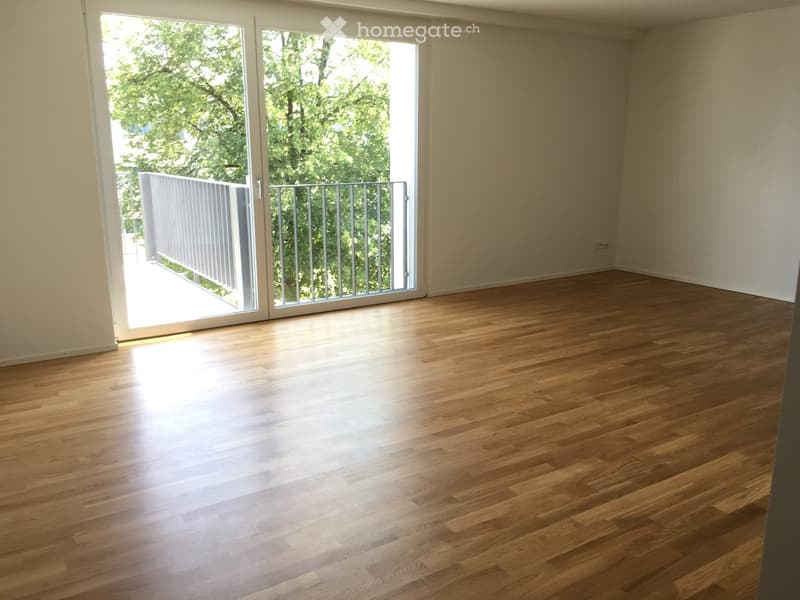 Empty room with wooden flooring and large sliding glass doors leading to a balcony with a metal railing.