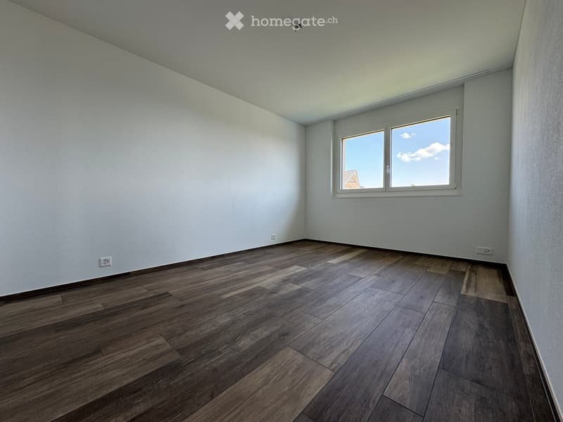 Empty room with wooden flooring and white walls, featuring a large window with white frame and a view of the sky.