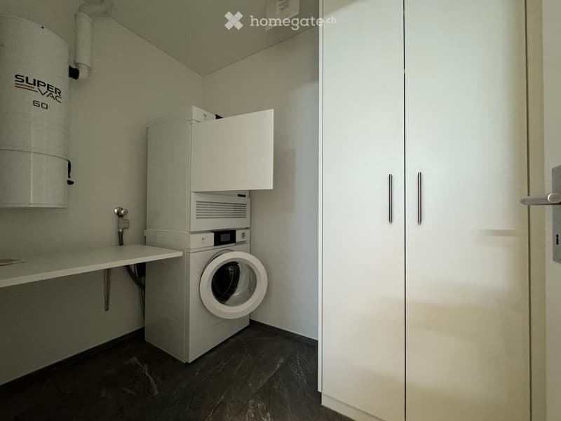 A small, well-lit room with a washing machine, dryer, and a small table with a cabinet above it.