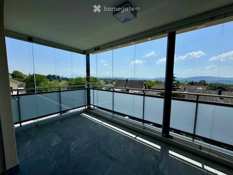 Modern balcony with large glass panels, tiled floor, and a scenic view of the countryside.