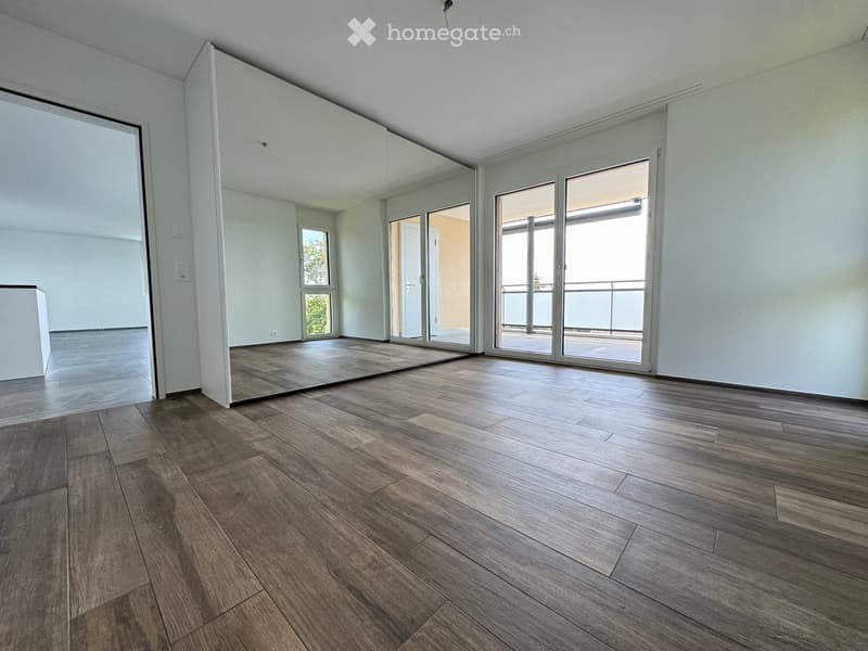 Empty room with wooden flooring, large sliding glass doors leading to a balcony, and white walls.