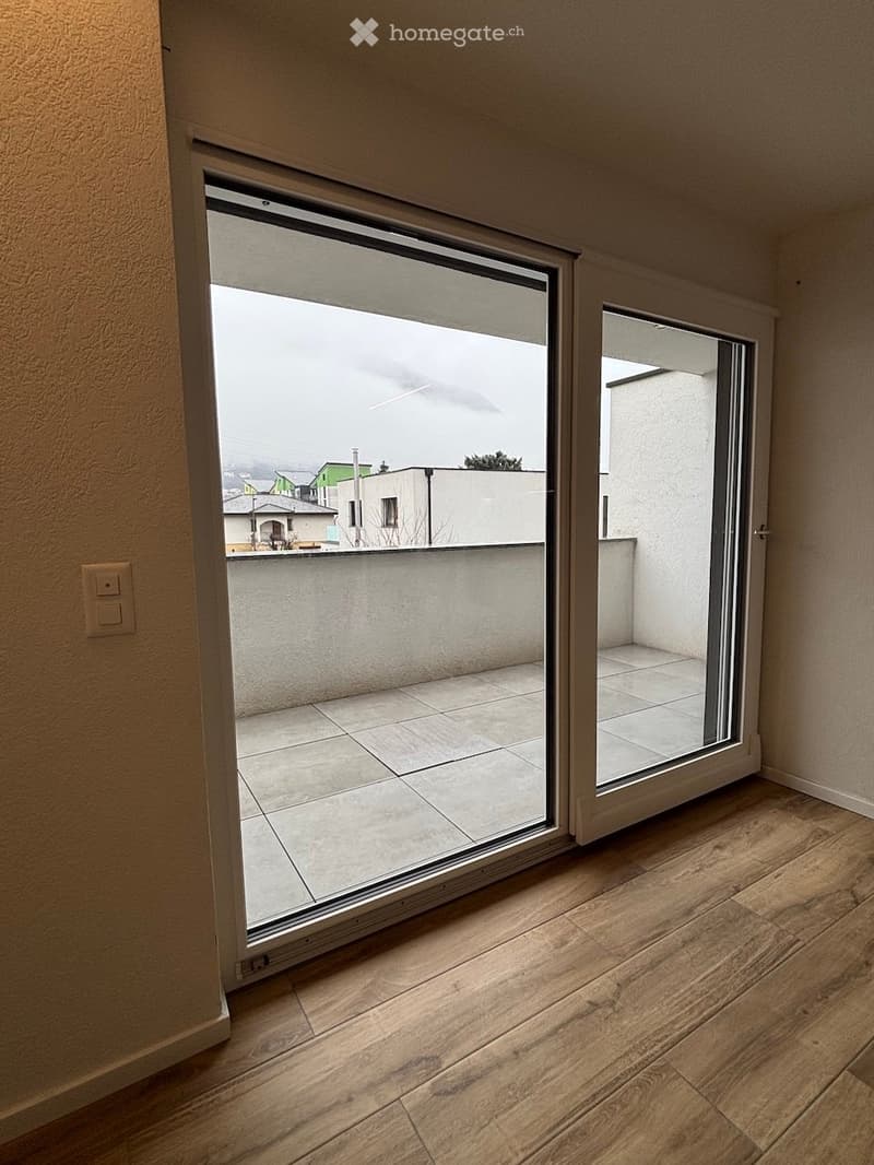 Empty room with wooden flooring and large sliding glass doors leading to a tiled balcony area.