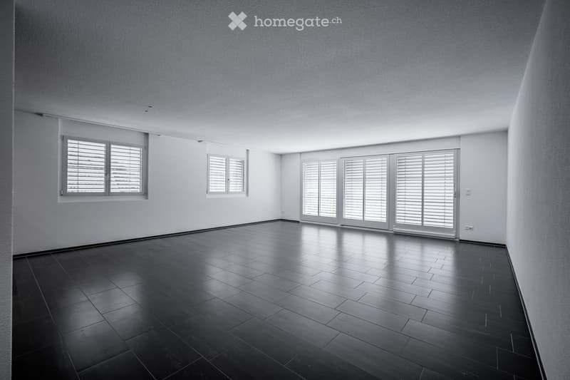 Empty room with dark tiled floor, white walls, and multiple windows with blinds. No furniture or equipment present.