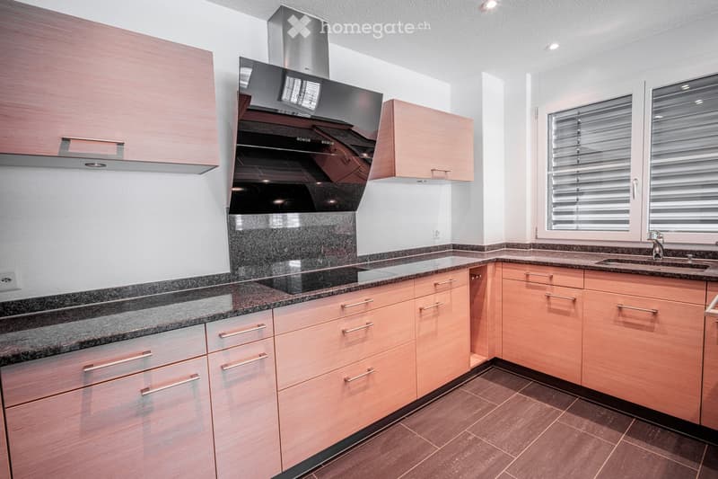 Modern kitchen with light wood cabinets, granite countertops, stainless steel range hood, and a sink with a modern faucet.