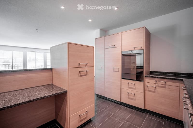 Modern kitchen with light wood cabinets, granite countertops, and a built-in oven.