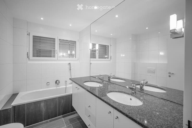 Modern bathroom with a bathtub, double sink vanity, and large mirror. The space features white tiled walls and a granite countertop.