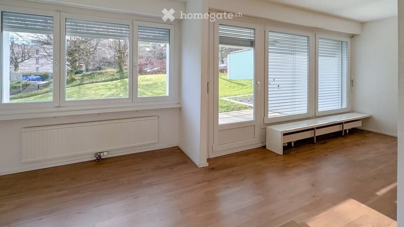 Empty room with wooden flooring, large windows with blinds, radiator, and a built-in bench along one wall.